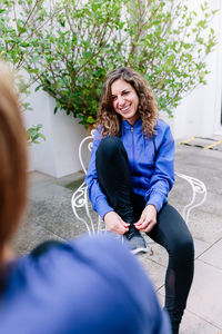 High angle view of smiling young woman tying sports shoe while sitting on chair