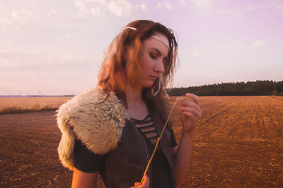 Portrait of young woman standing on field against sky