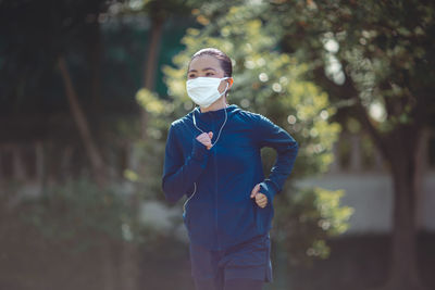 Woman running while wearing mask against trees