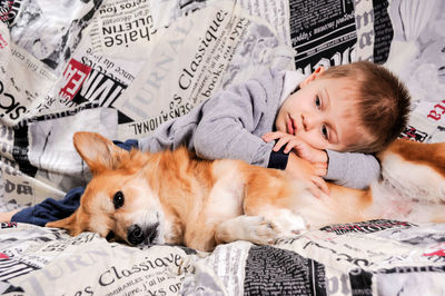 Cute boy lying with dog on bed at home