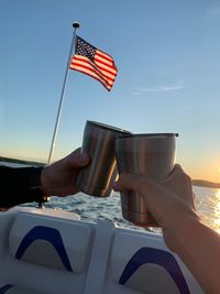 Low angle view of hand holding flag against sky