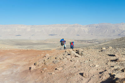 Rear view of men walking on desert against clear sky