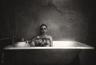 Sad woman sitting in bathtub against wall