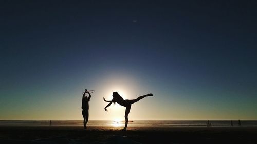 Silhouette people dancing at beach against clear sky during sunset