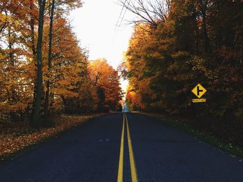 Road amidst autumn trees against sky