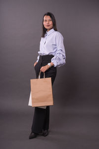 Portrait of a smiling young woman standing against gray background
