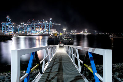 Illuminated city by sea against sky at night