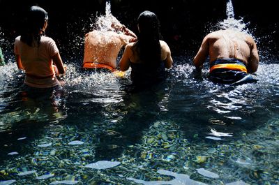 Rear view of people enjoying waterfall at resort