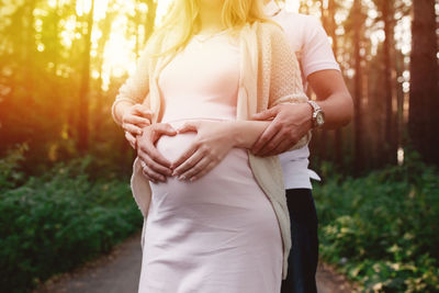 Midsection of man with pregnant wife making heart shape on belly