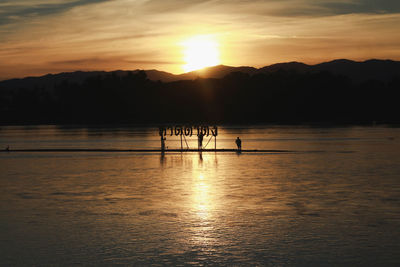 Silhouette people in lake against sky during sunset