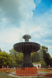 Fountain in park against cloudy sky