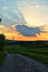 Road amidst field against sky during sunset