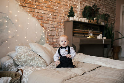 Portrait of boy sitting on bed at home