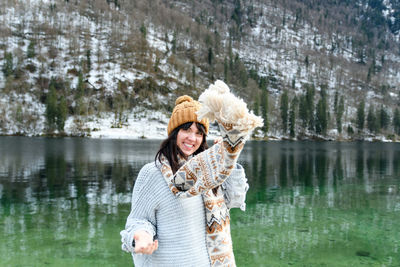 Young woman in winter sweater smiling, standing by a lake.