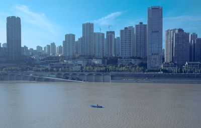 Modern buildings by river against sky in city