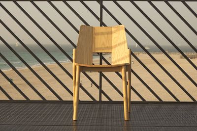 Close-up of chair on by fence against sea