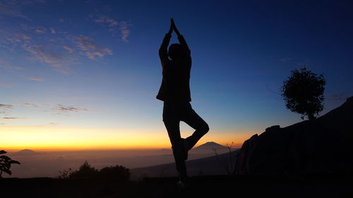 Silhouette man doing yoga against sky during sunset