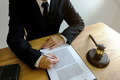 Midsection of lawyer with pen and document sitting at desk