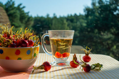 Rose hip tea and wild rose fruits in a bowl. view from window in the background.