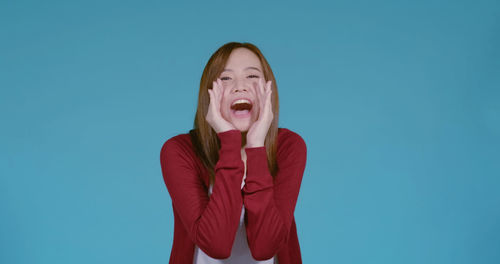 Portrait of young woman standing against blue background