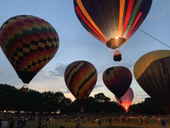 High angle view of people looking at illuminated hot air balloons on land against sky