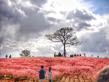 Rear view of people walking on field against sky