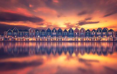 Buildings reflecting on calm lake during sunset in city