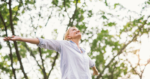 Low angle view of woman with arms outstretched against trees