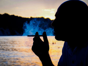 Portrait of silhouette man photographing by lake against sky during sunset