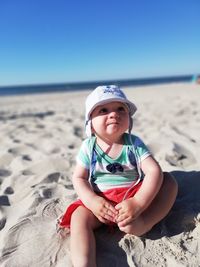 Cute boy sitting on sand at beach against sky