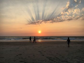 Silhouette people on beach against sky during sunset