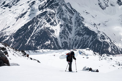 Young woman athlete with a backpack and a snowboard on her back climbs backcountry uphill on a snowy