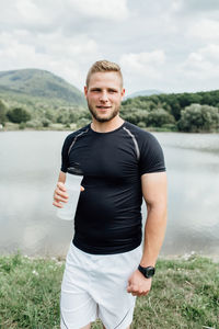 Young man drinking water against lake