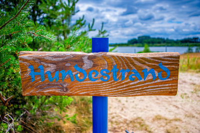 Close-up of sign board on tree against sky