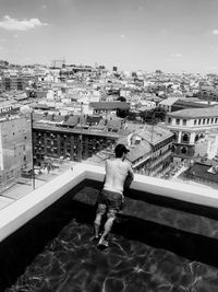 Rear view of man standing by swimming pool against buildings in city