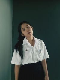 Portrait of teenage girl wearing school uniform against wall