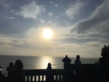Silhouette people overlooking calm sea at sunset