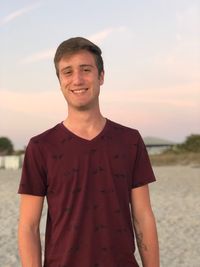 Portrait of smiling young man standing on beach against sky