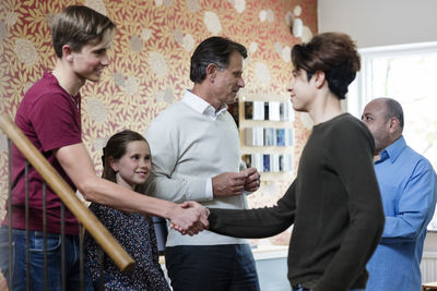 Multi-ethnic friends shaking hands while family greeting in living room