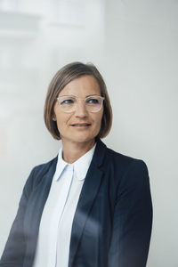 Mature businesswoman wearing eyeglasses in front of white wall