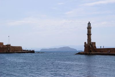 Lighthouse on building by sea against sky