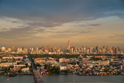 Modern buildings by river against sky during sunset