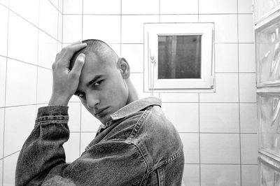 Side view portrait of young man standing by wall in bathroom