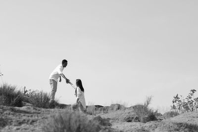 Man assisting woman on land against clear sky