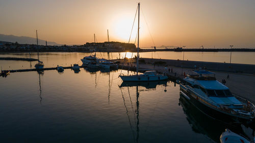 Boats moored in harbor at sunset