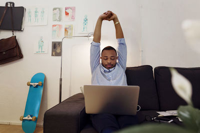 Tired businessman stretching hands while working on laptop in creative office