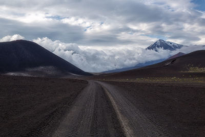 Dirt road amidst landscape and mountains against sky