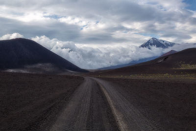 Dirt road along landscape and mountains against sky