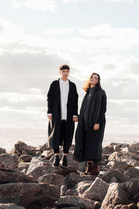 Portrait of lesbian women holding hands while standing on rock against sea and sky