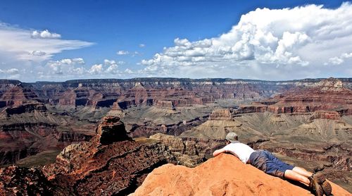 Man lying on rock formation at grand canyon against sky